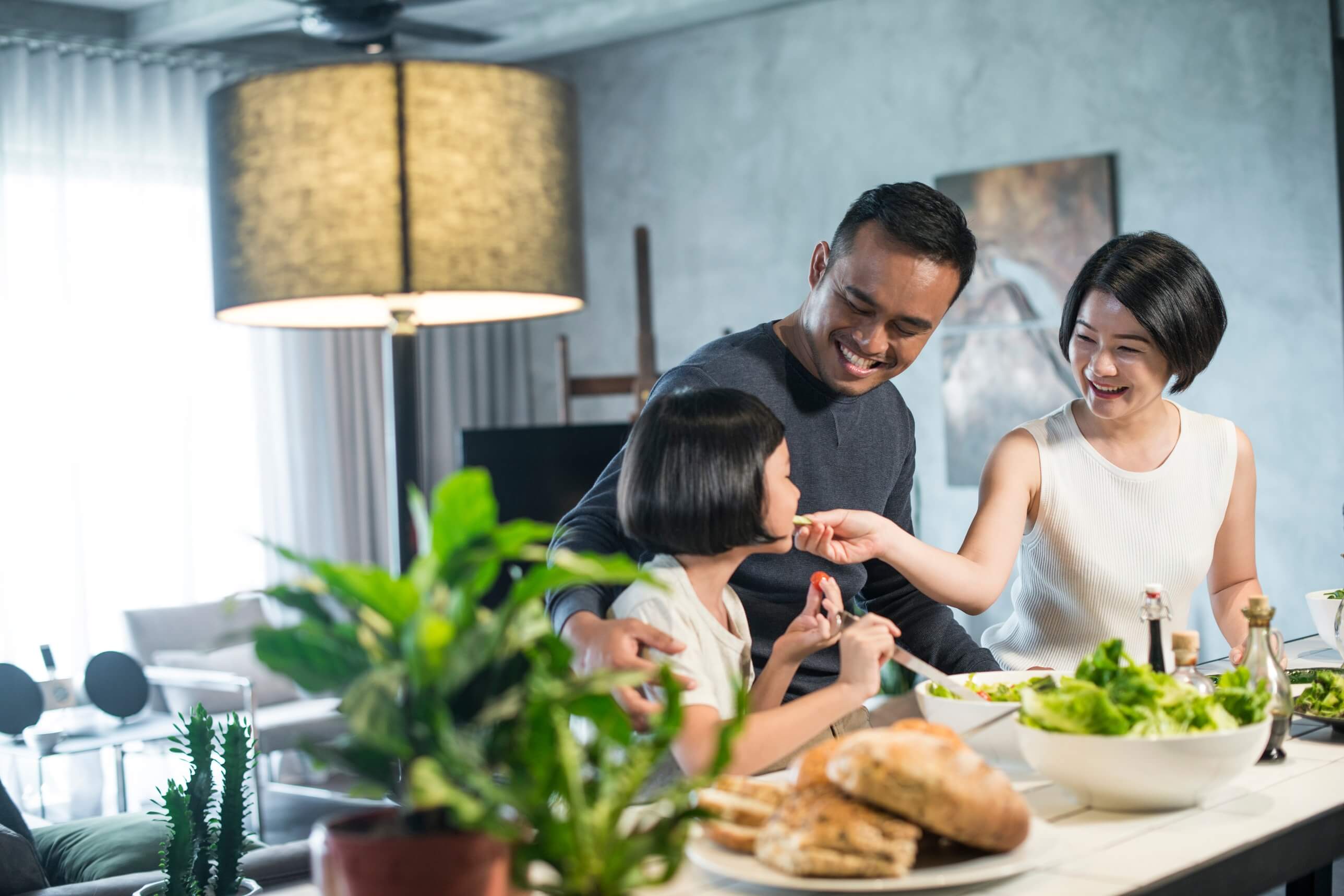 A couple with their young daughter sat at the kitchen counter making a salad