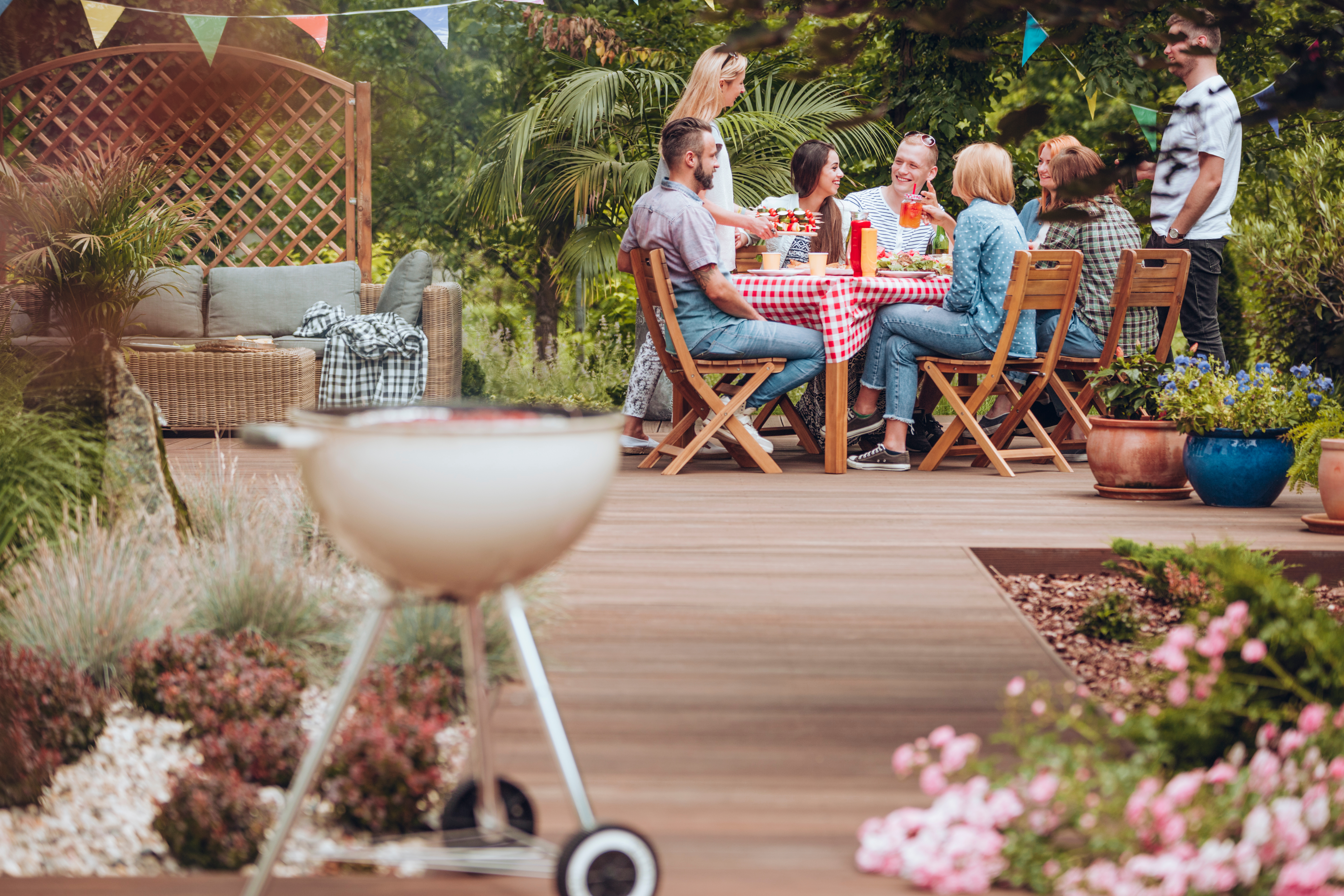 A group of friends at around a table on their garden decking having a barbecue
