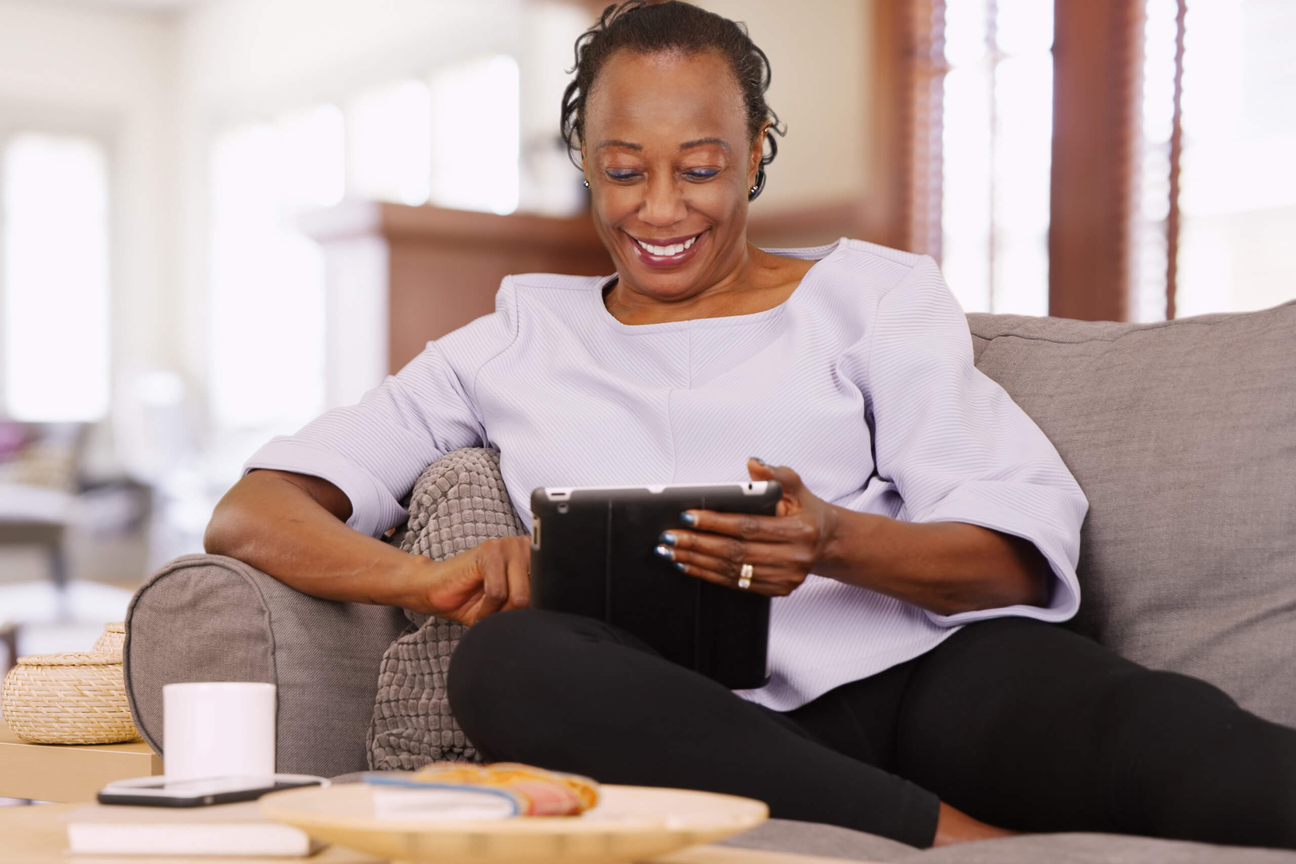 A smiling woman sitting on a sofa reading her survey report on an iPad