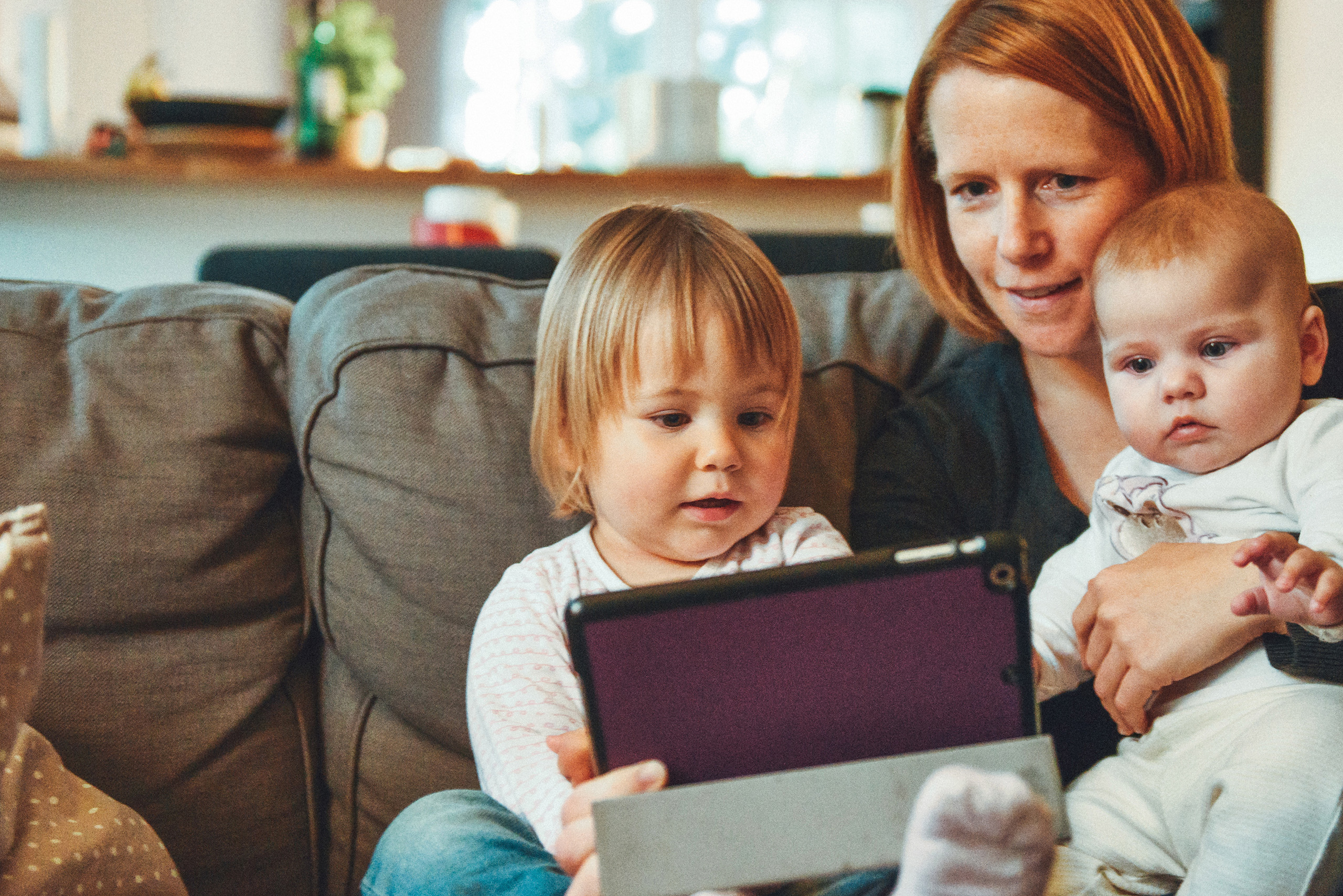 A young woman with two children sat on a sofa looking at insurance policies on an iPad