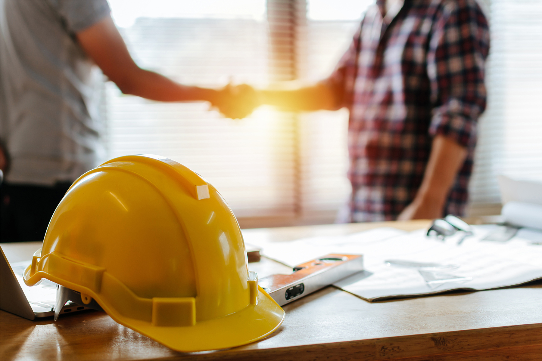 Close up of a hard hat on a table and two people shaking hands in the background